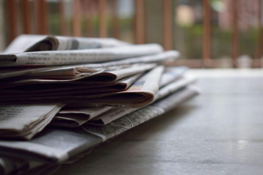 Stack of folded newspapers on a table with a soft-focus background.