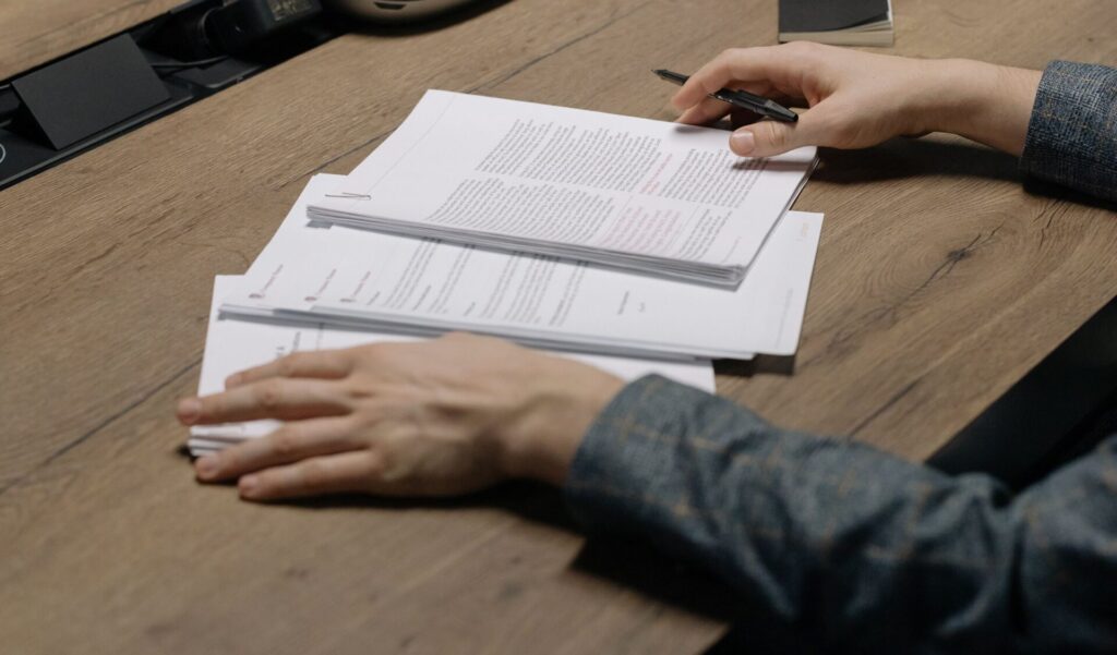 Close-up of a person reviewing printed documents with a pen at an office desk.