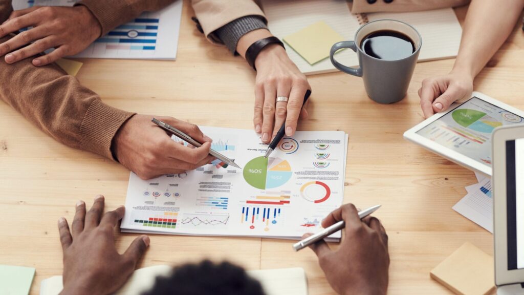 Colleagues at a wooden table reviewing printed charts and a tablet with graphs during a business meeting.